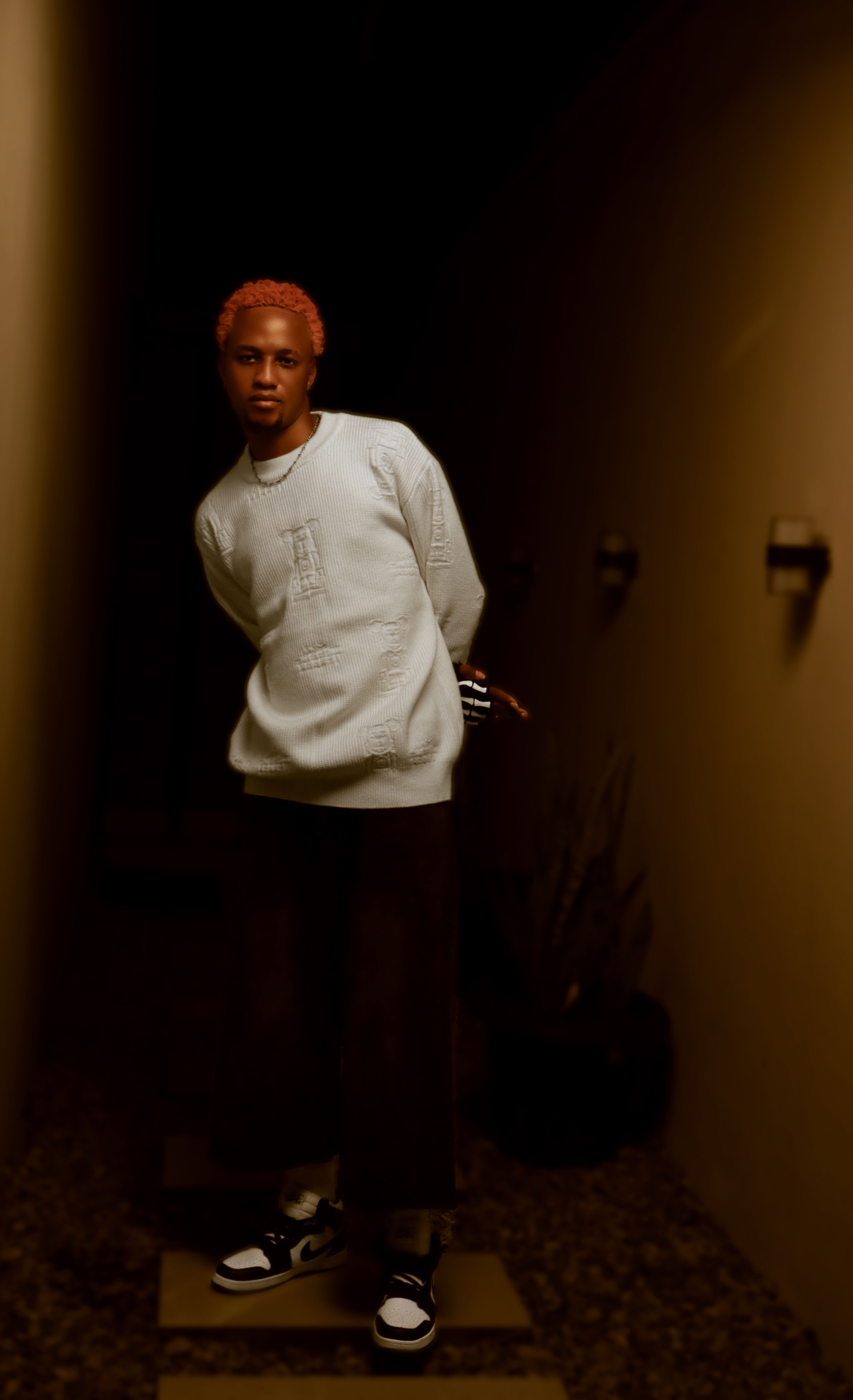 Portrait of a fashionable young adult with stylish attire in a dimly lit hallway setting.