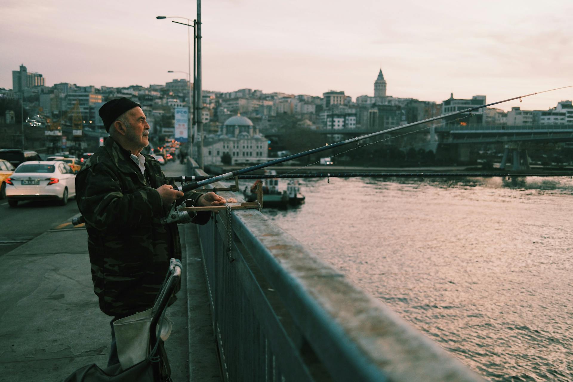 A man fishing on a bridge with the Galata Tower in the background during sunset in Istanbul.