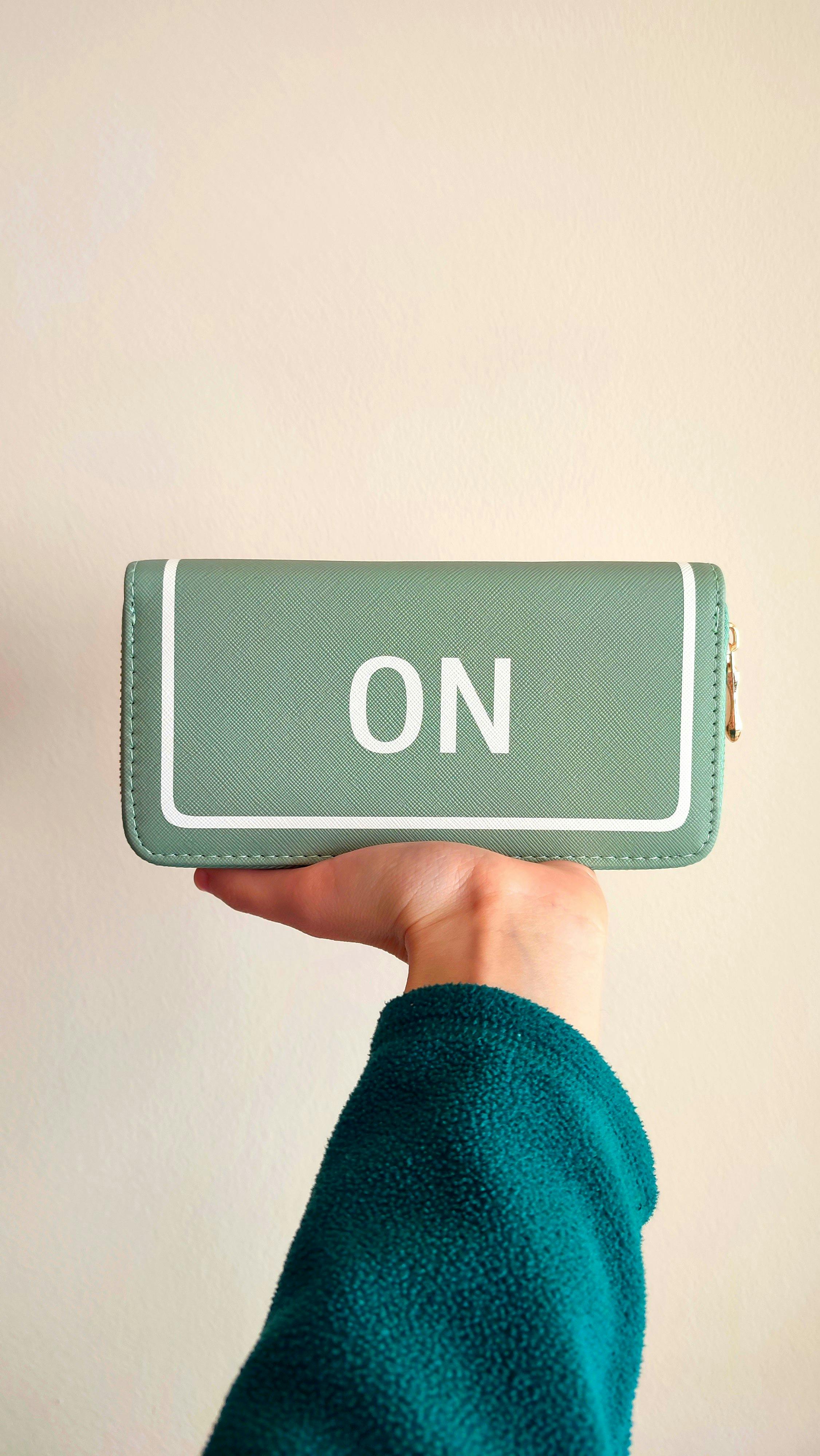 grátis Uma mão segurando uma bolsa minimalista verde menta contra um fundo neutro. Foto profissional