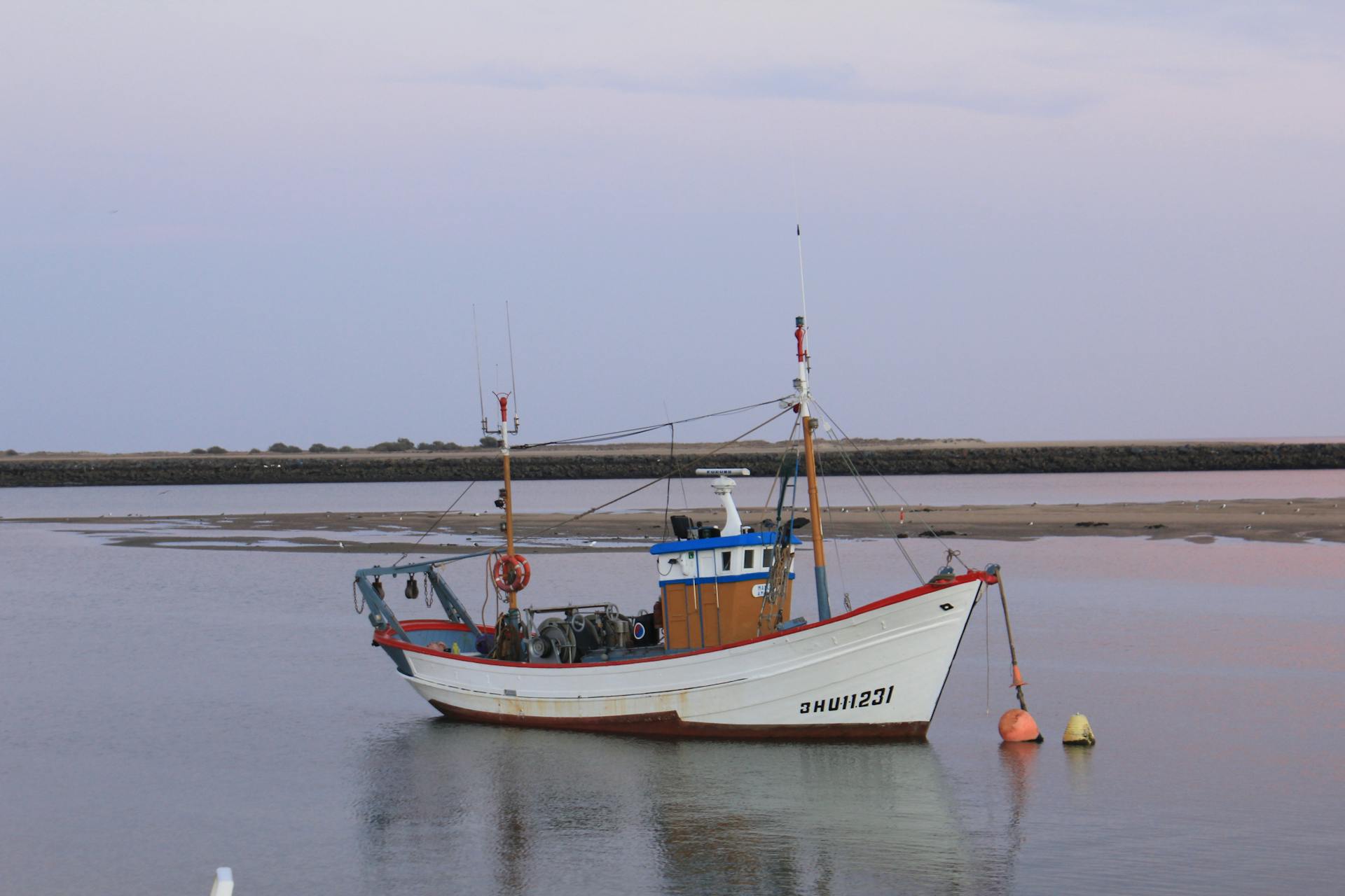 A fishing boat rests calmly on serene waters with a soft pastel sky backdrop.