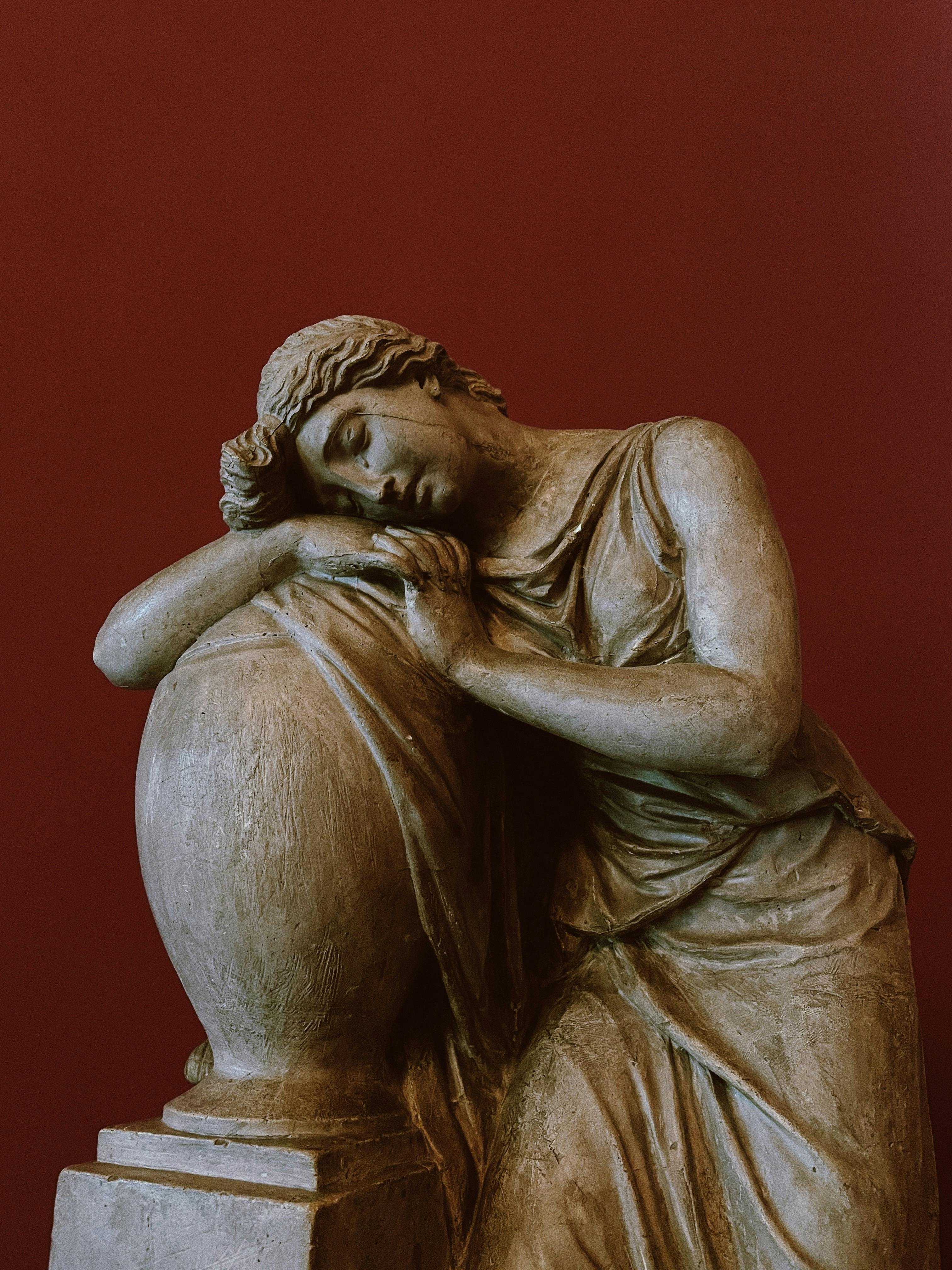 Photograph of a classical Greek statue against a rich red background, highlighting ancient art.