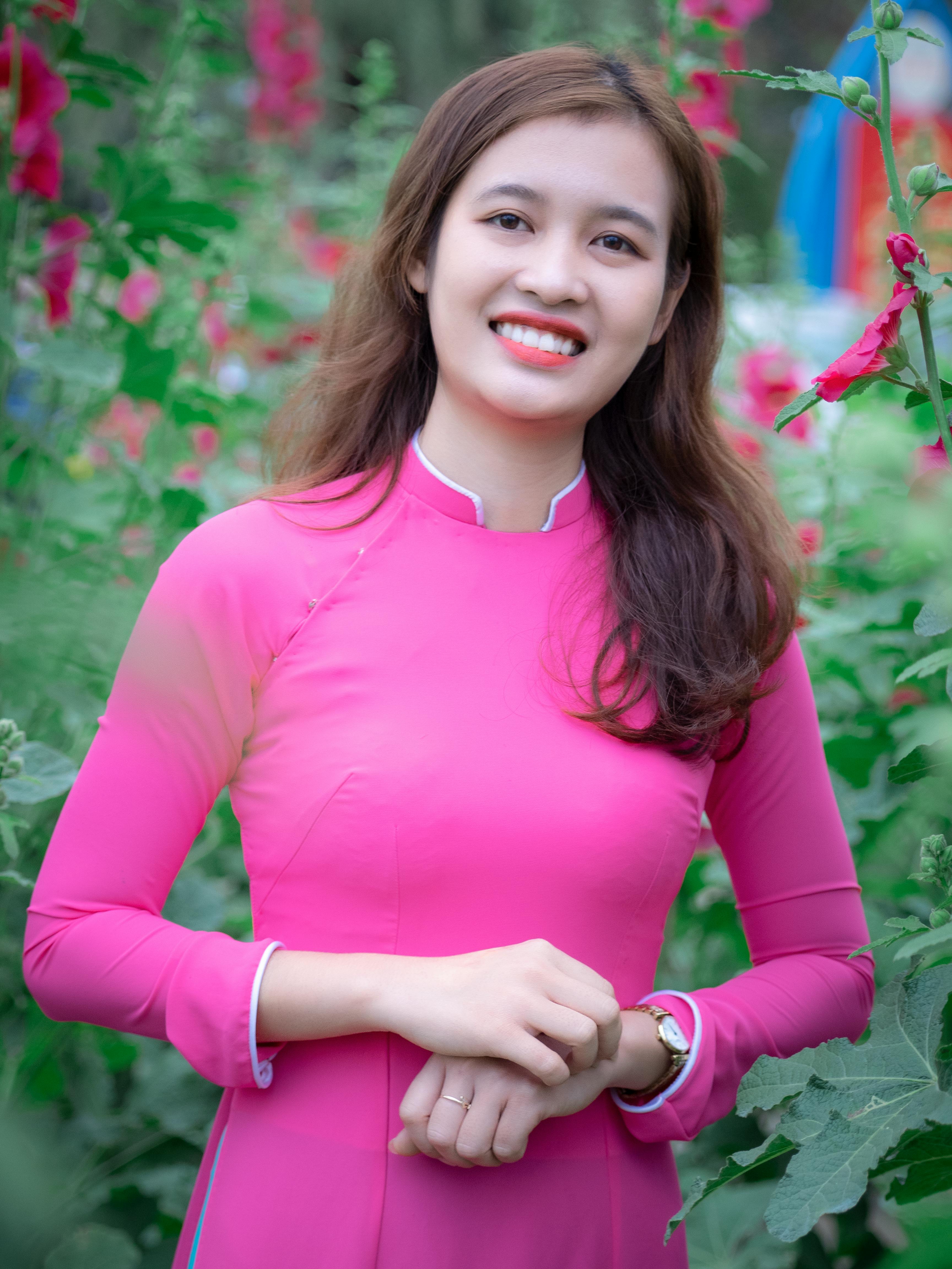 Smiling woman in pink Ao Dai surrounded by flowers, capturing Vietnamese culture and beauty.