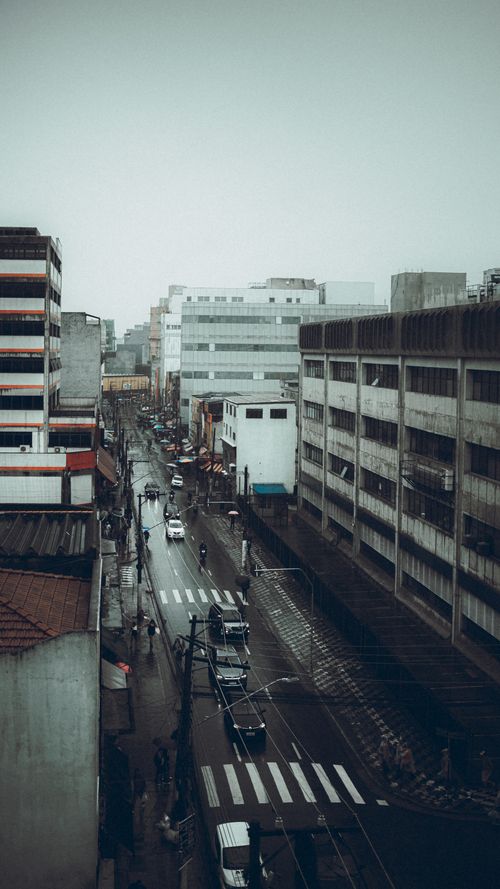 Free A moody urban street view with wet roads and a cloudy sky in a busy city. Stock Photo