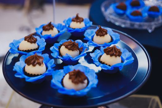 Array of sweets with chocolate topping in blue wrappers on a tray.