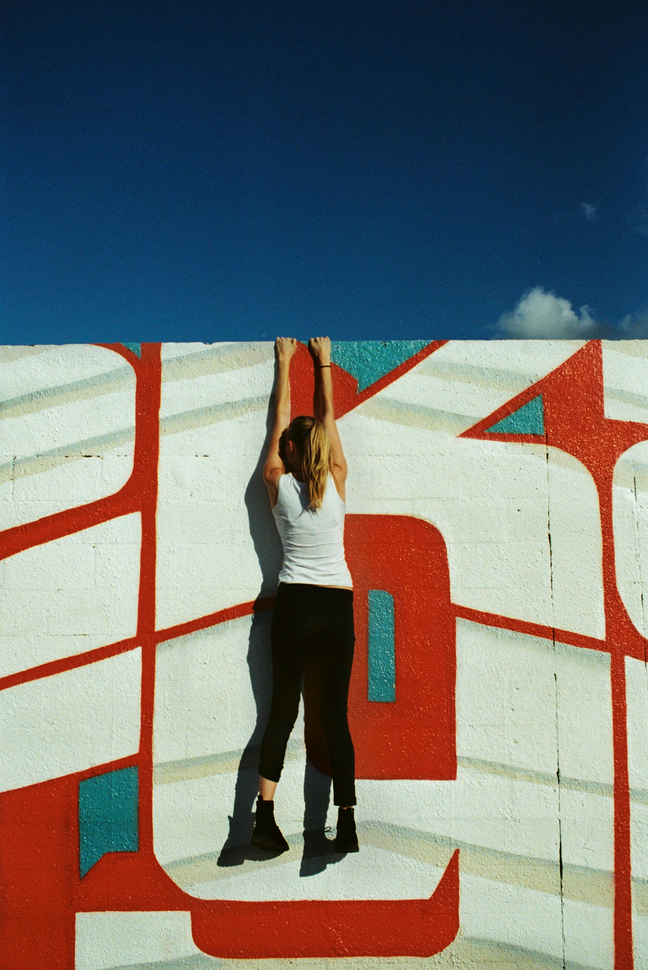 一名女子在晴朗的蓝天下，背影正攀爬着充满活力的壁画