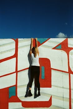 一名女子在晴朗的蓝天下，背影正攀爬着充满活力的壁画
