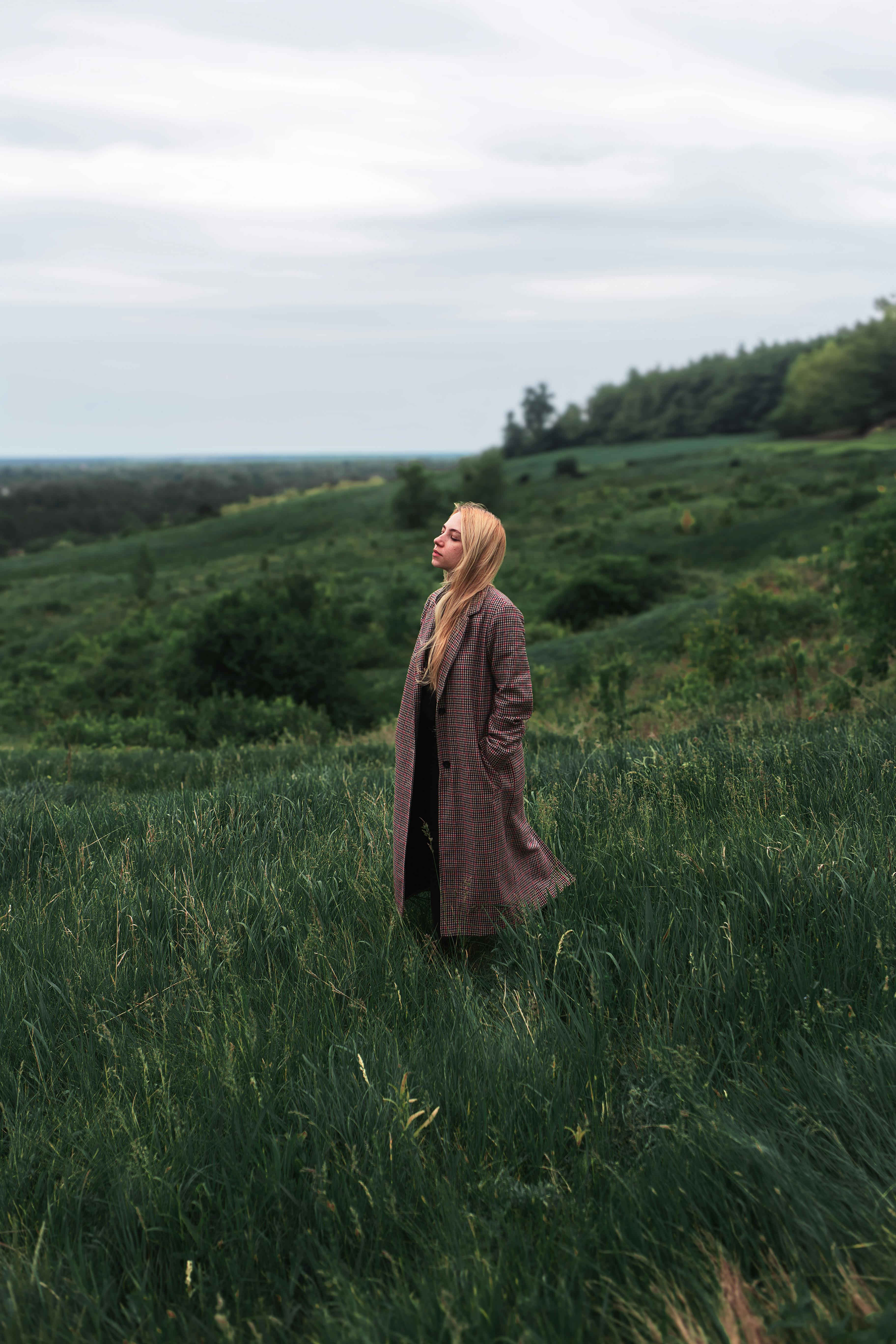 A serene portrait of a woman in a coat standing alone in a lush green field.