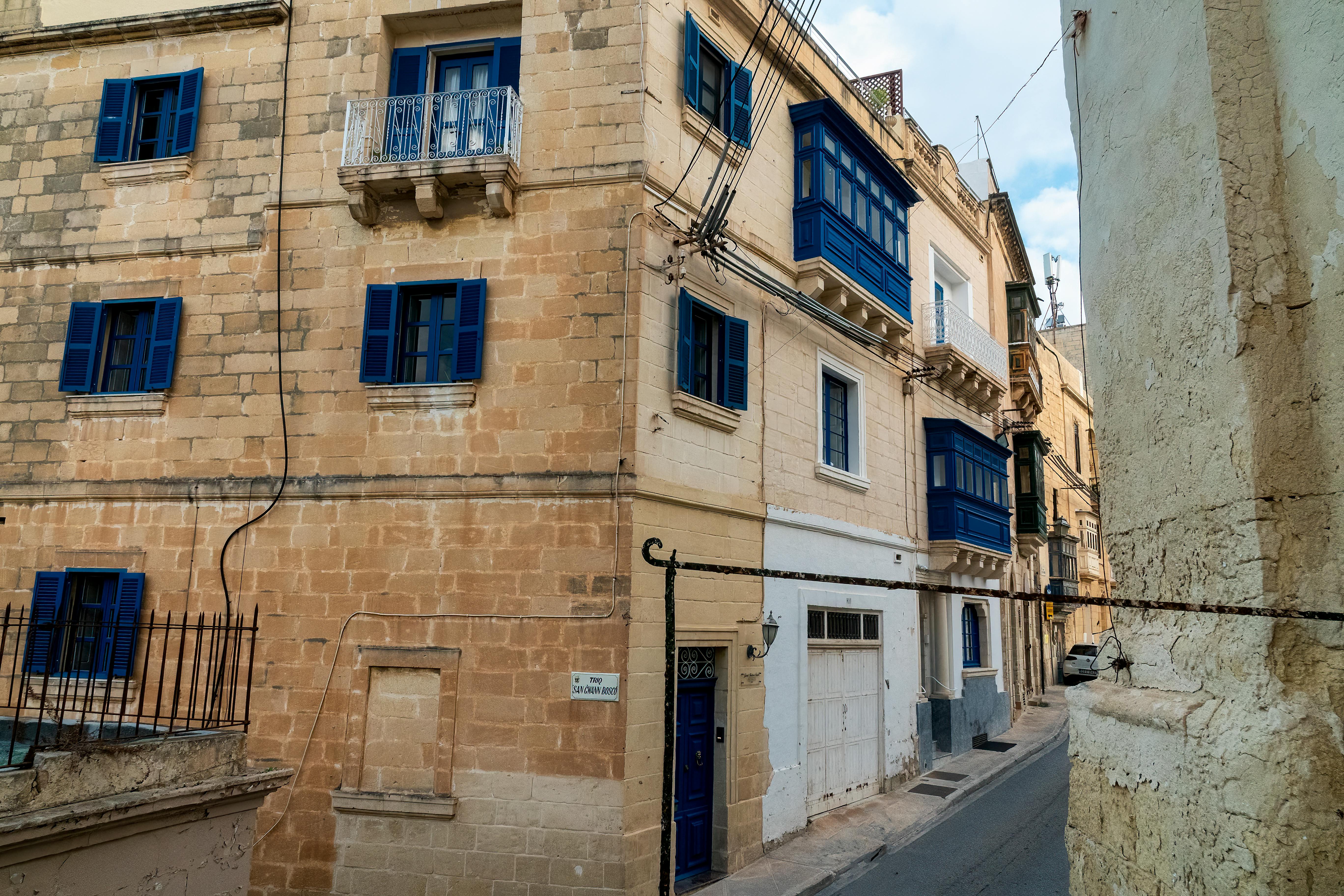 Traditional Maltese street with limestone buildings and blue shutters in a narrow lane.
