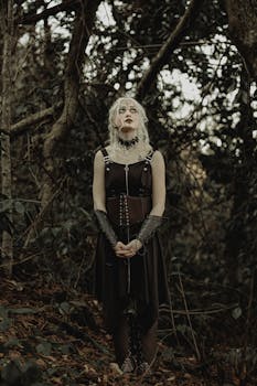 A gothic woman stands solemnly in an eerie forest, exuding mystery and elegance.
