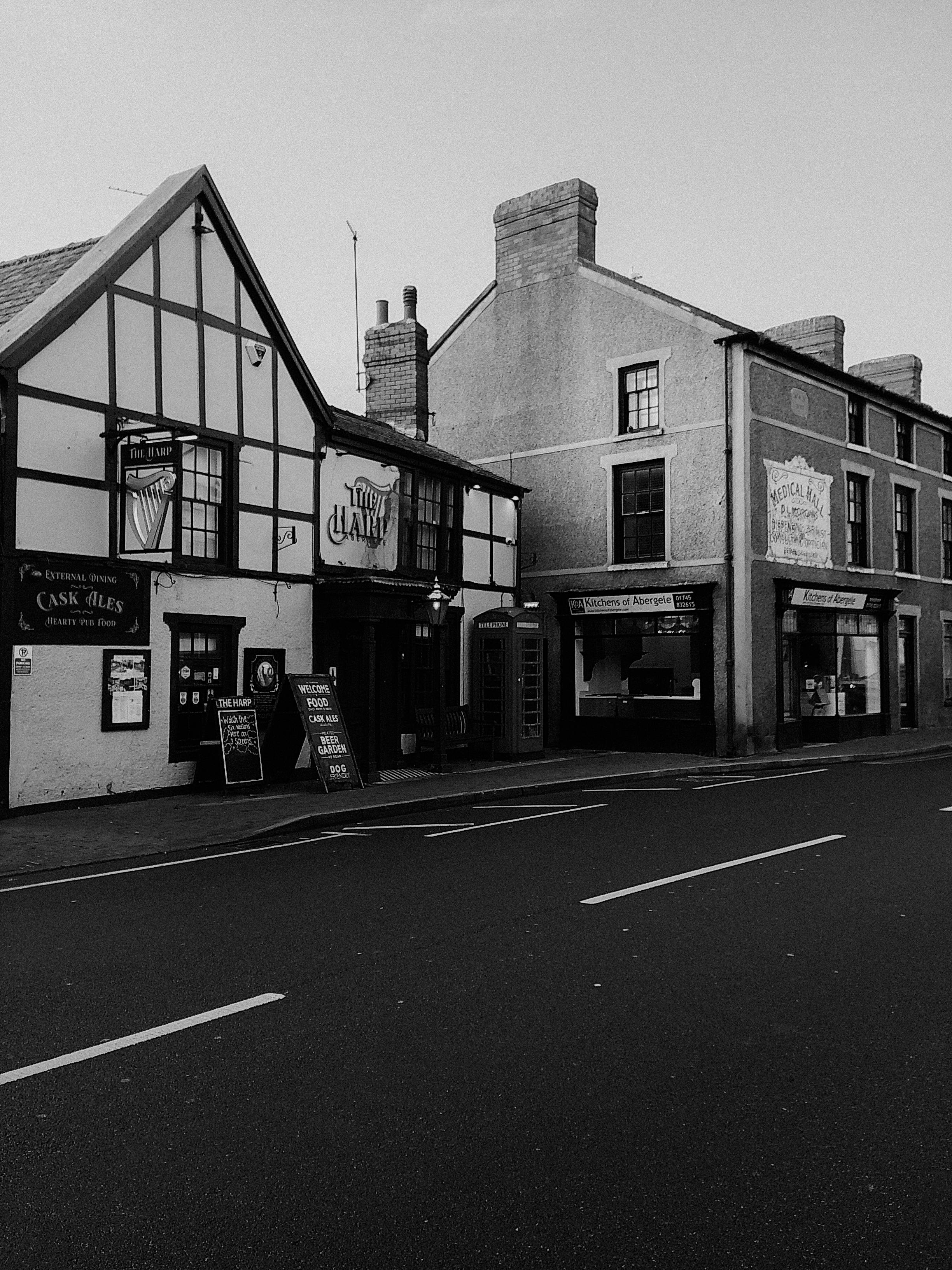 Historic street in black and white with vintage shopfronts and pub, offering a nostalgic view.