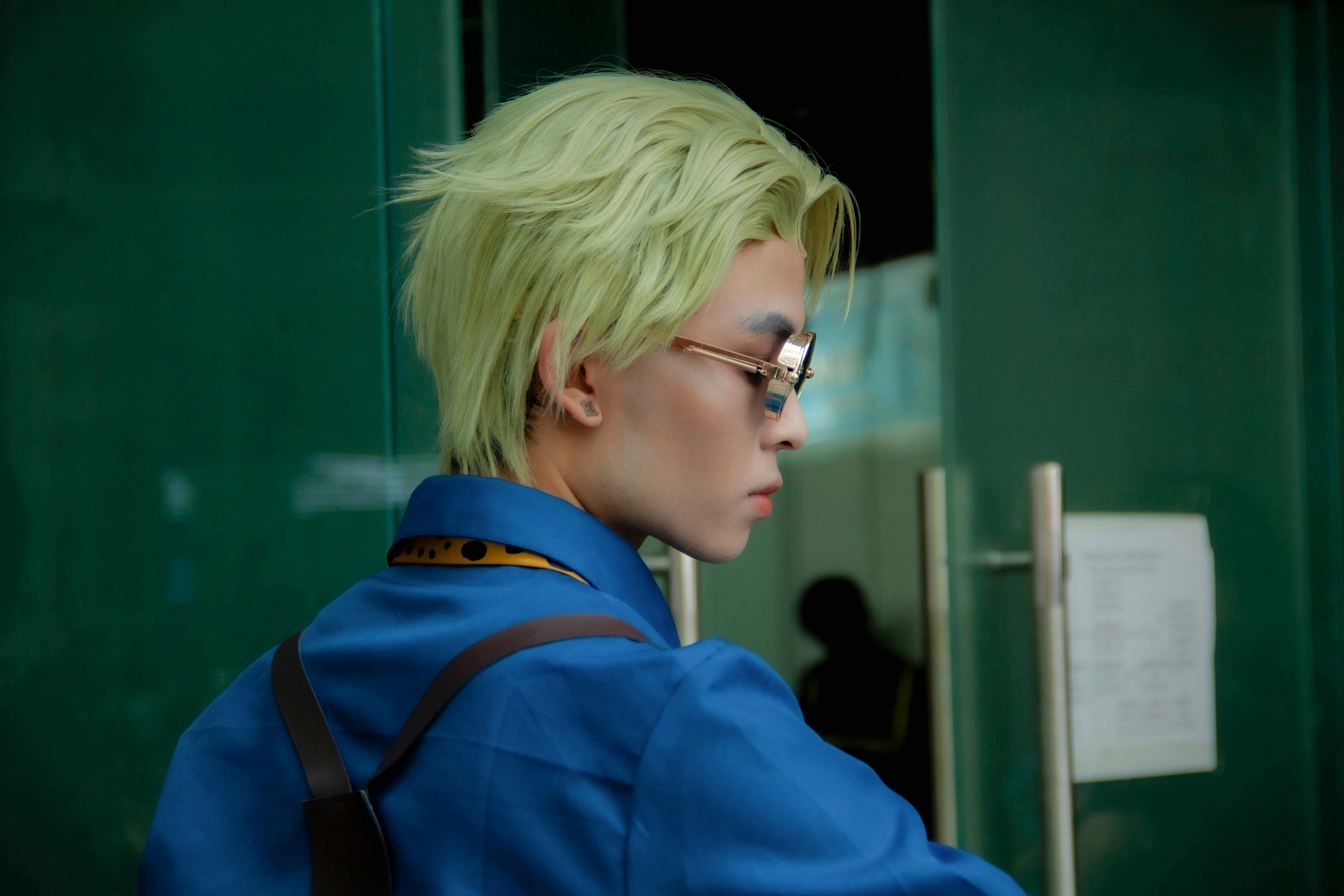 Stylish person with blonde hair and glasses in a blue outfit, showcasing modern fashion.