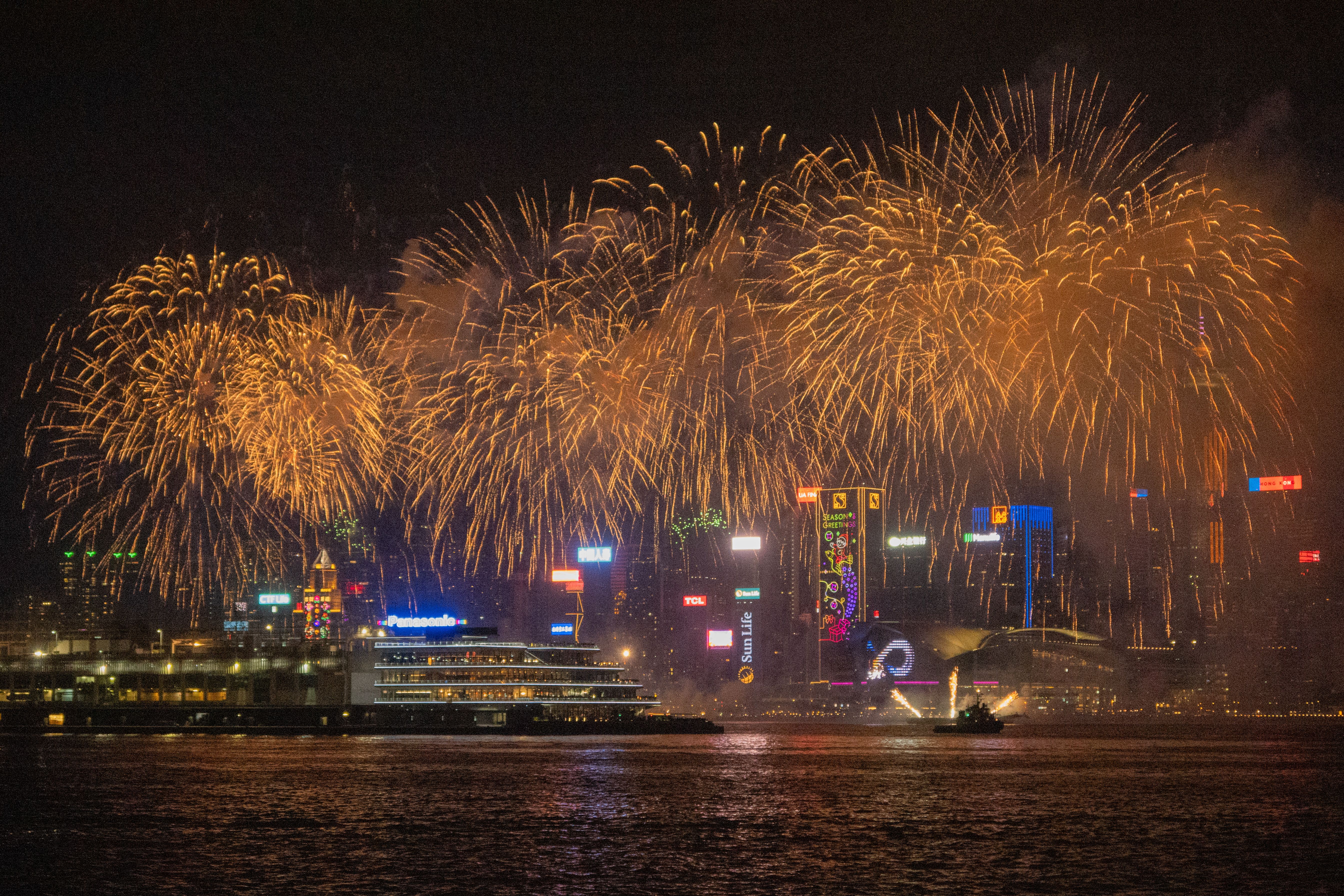 Spectacular fireworks display over Hong Kong's Kowloon skyline at night, showcasing vibrant city lights and reflections.