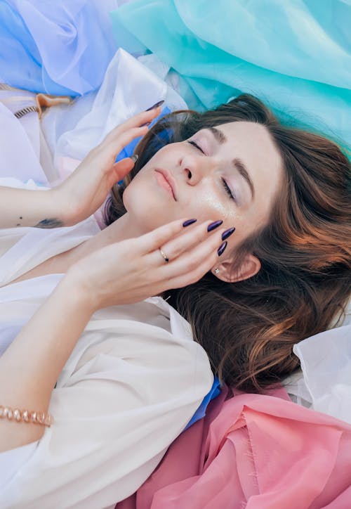 Женщина в белом топе лежит на разноцветных тканях