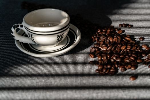 Ceramic coffee cup with coffee beans lit by afternoon sunlight on a textured surface.