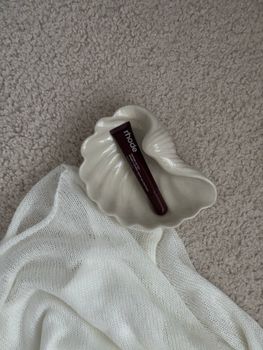 A skincare product tube elegantly placed in a ceramic shell dish on textured fabric.