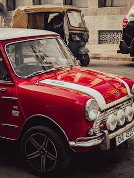 Classic red Mini Cooper car parked on a city street with a tuk-tuk in the background.