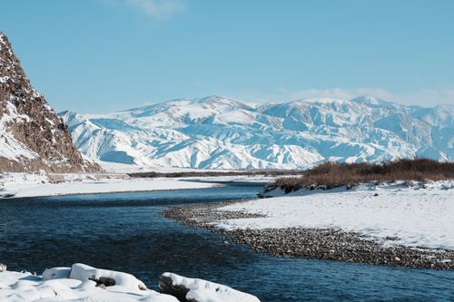 Free Serene winter mountain landscape with a flowing river and snow-covered peaks. Stock Photo
