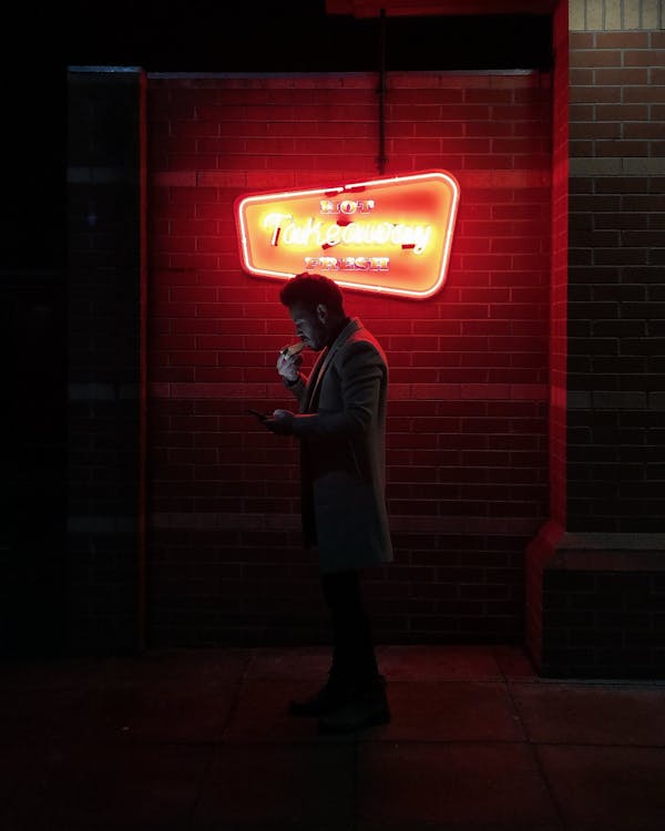 Silhouette of Person Standing Near A Neon Light Signage
