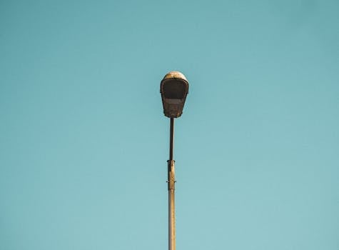 A lone street lamp set against a clear blue sky in a minimalist style.