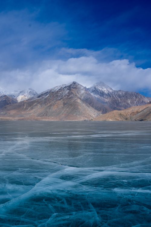 Free Gorgeous view of a frozen lake with snow-capped mountains under a clear blue sky. Stock Photo