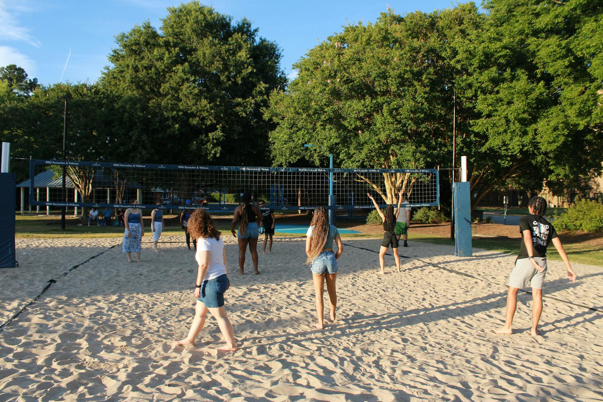 A group of teenagers playing beach volleyball in a sunny Norfolk, Virginia park.