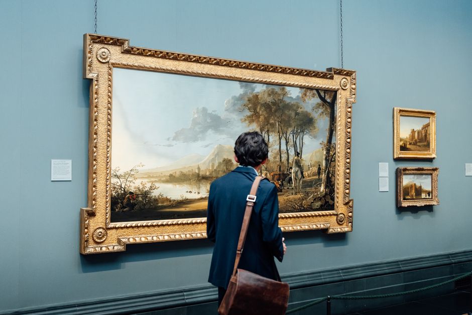 イギリスの美術館で、男性が額に入った大きな絵画を鑑賞している。