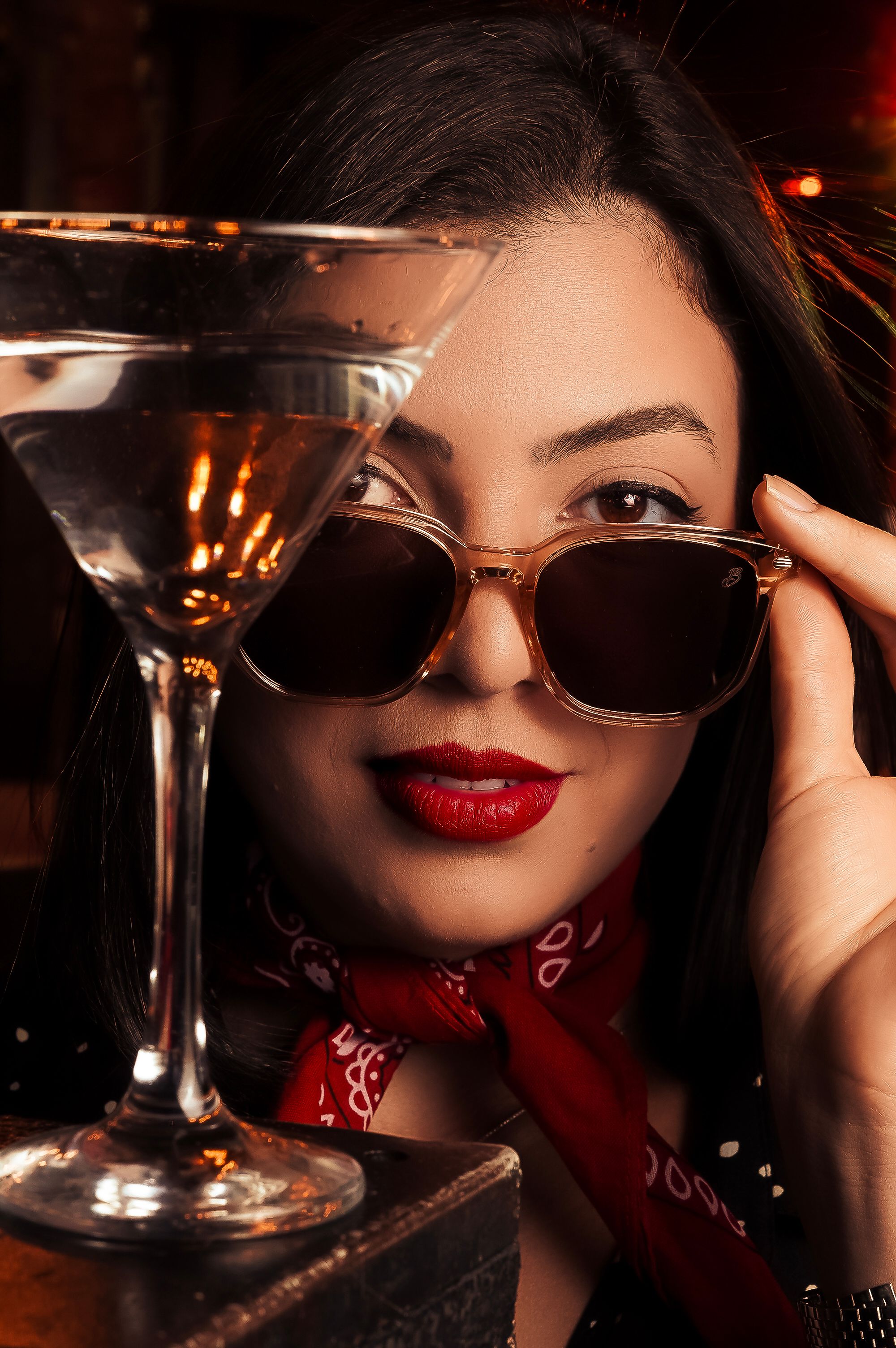 Chic woman wearing sunglasses with a martini glass at a trendy bar setting.