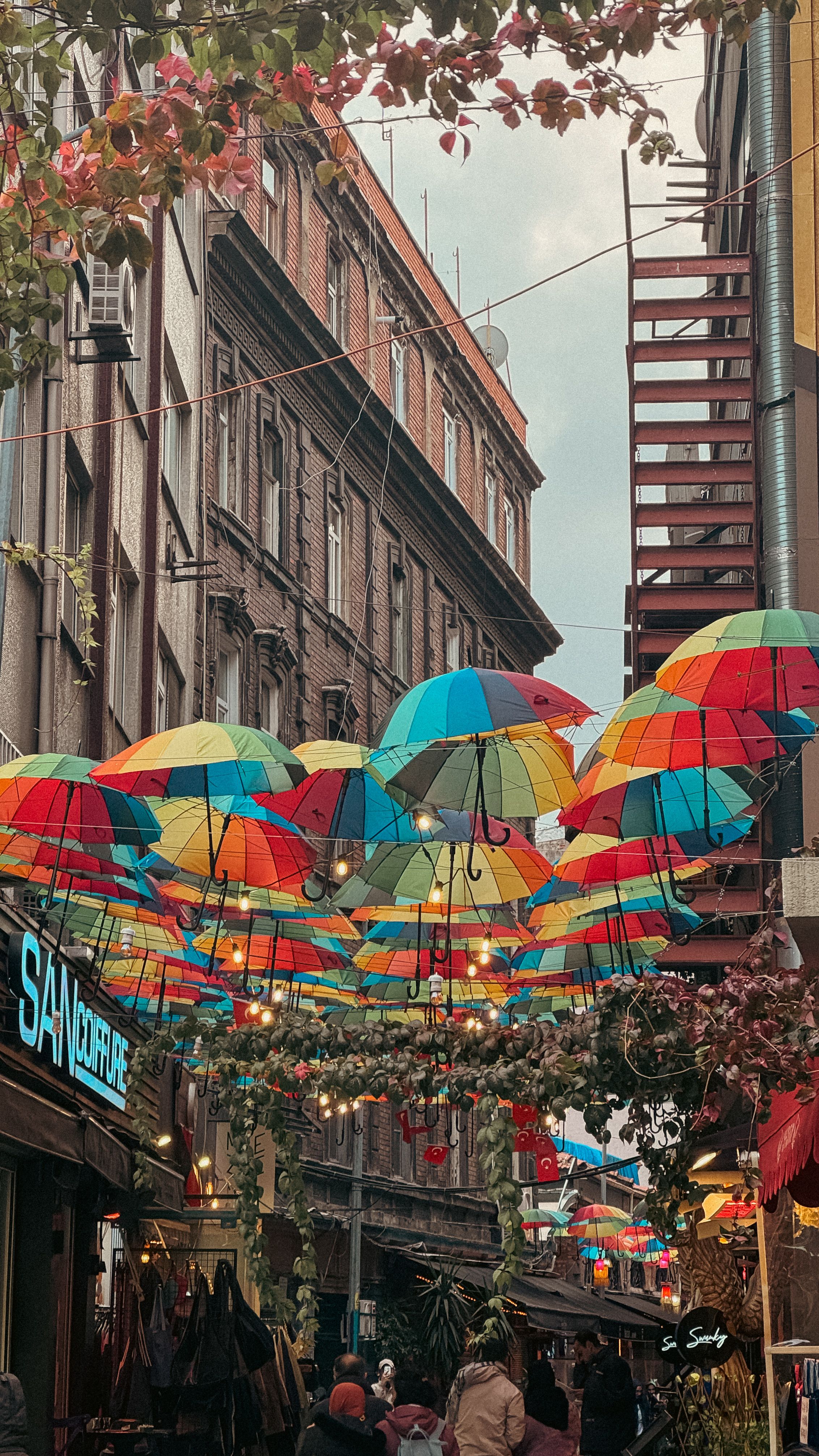 Vibrant umbrellas decorate a cozy street with rustic buildings and lively ambiance.