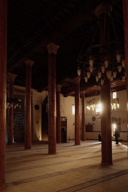 Free Dimly lit interior of an ancient mosque with tall wooden columns and chandeliers. Stock Photo