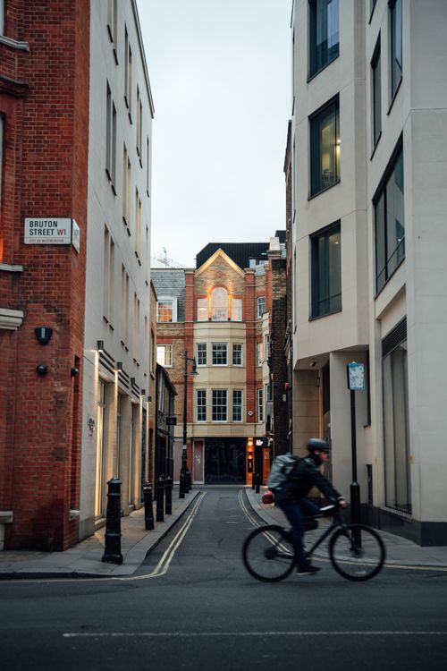 Free Cyclist rides through Bruton Street, showcasing London's urban architecture. Stock Photo