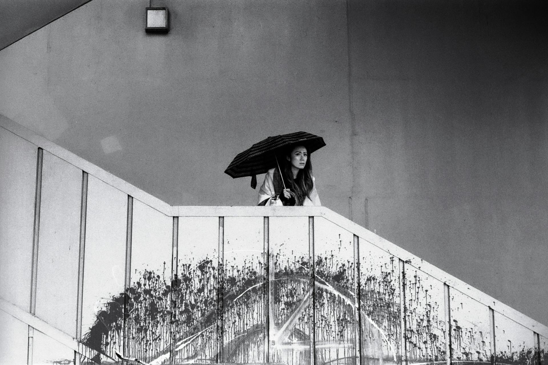 Black and white photo of a woman with an umbrella on a staircase in İstanbul, Türkiye.