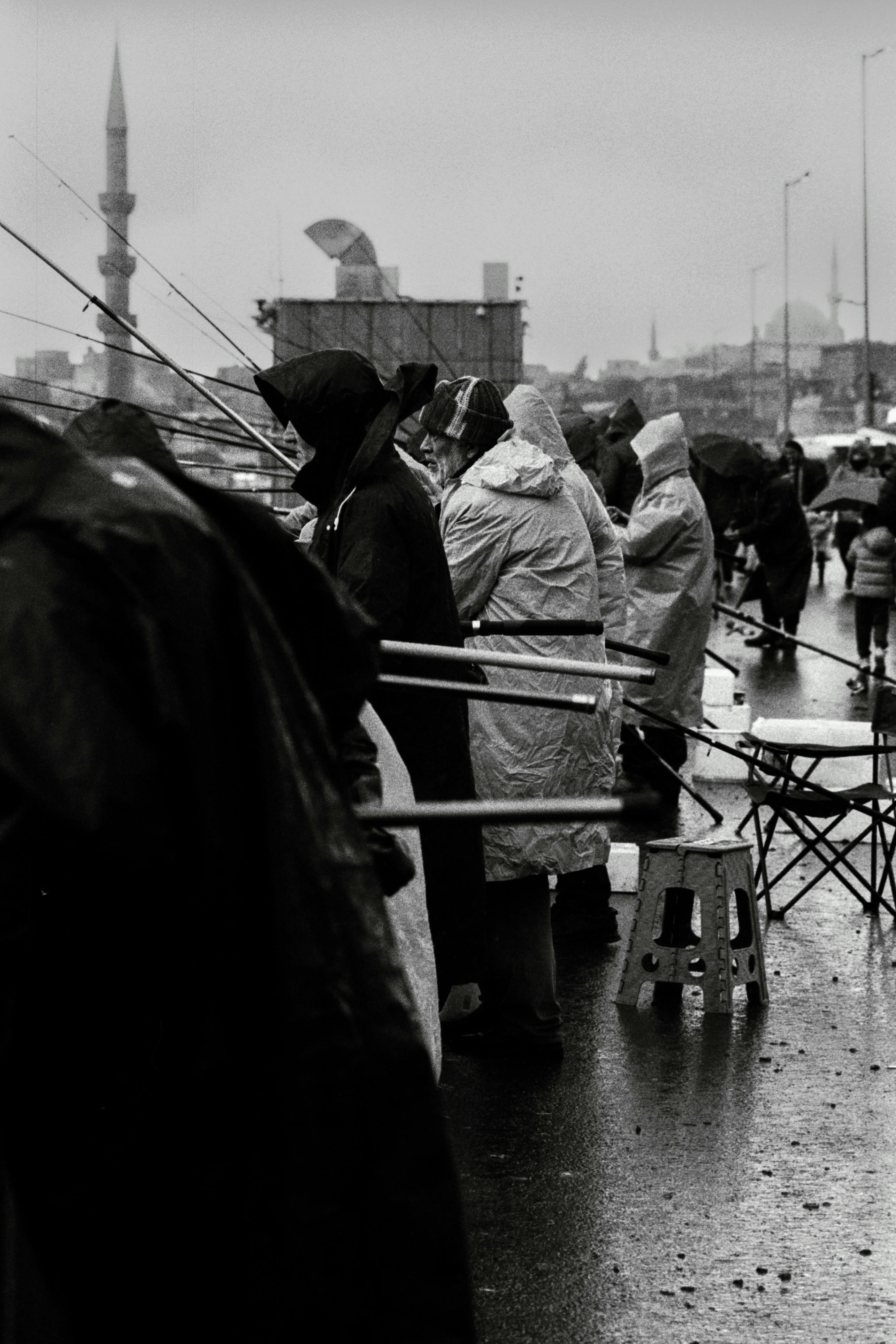 People fishing on a rainy day in İstanbul, Türkiye with iconic mosque in the background.