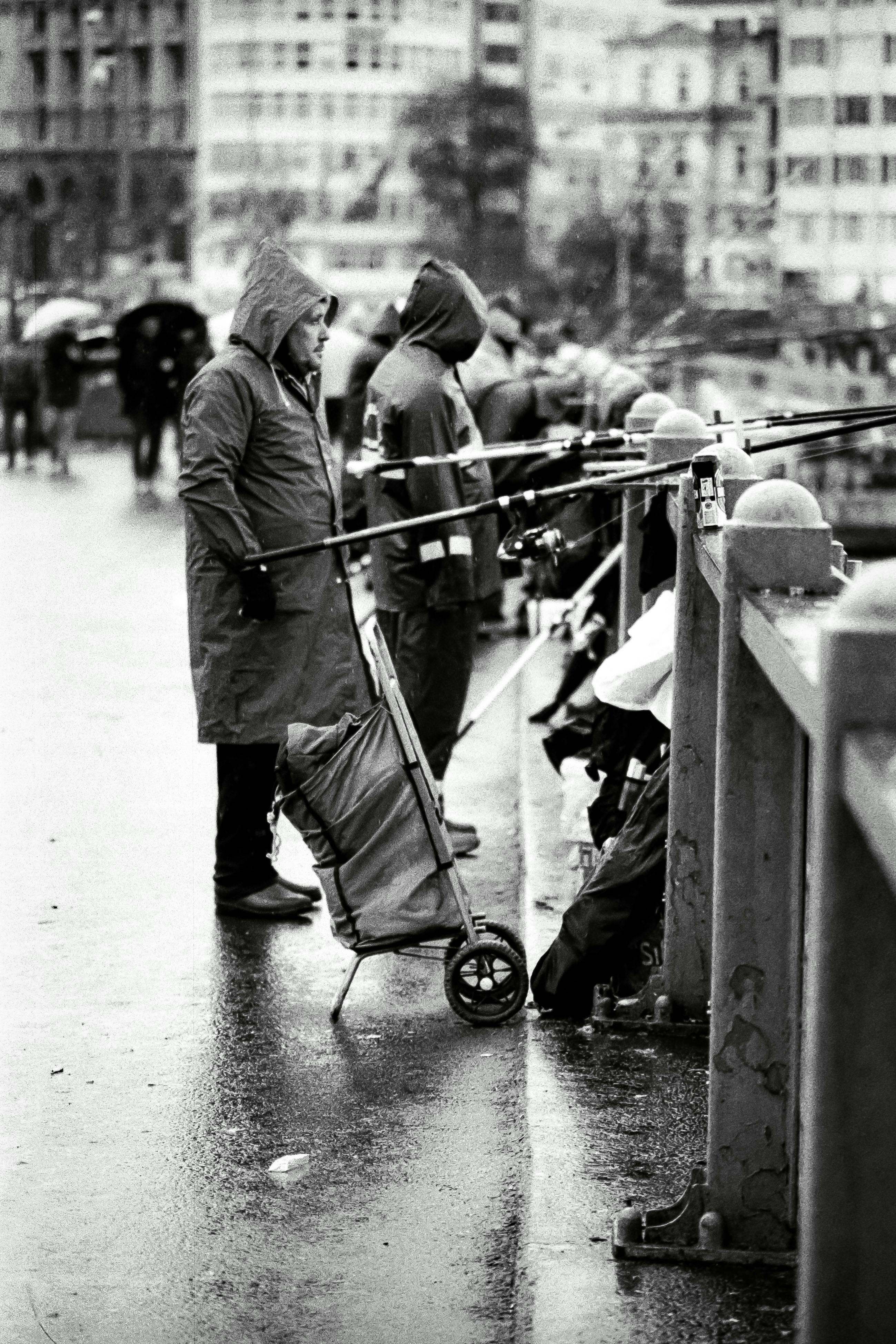 Monochrome image of fishermen in raincoats fishing on a rainy day in Istanbul.