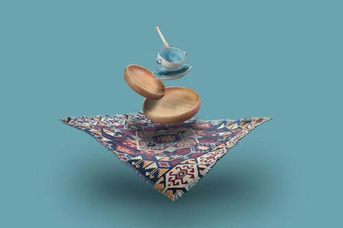 Various plates and teacup with spoon levitating over ornamental tablecloth against blue background