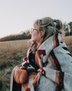 Woman Wrapped In A Printed Wool Blanket And Mittens Out In The Grass Field