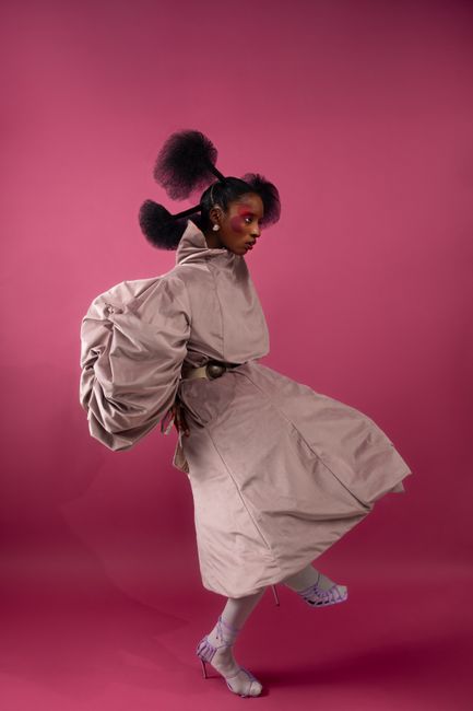 A model posing in a creative outfit on a pink backdrop showcasing modern fashion style.