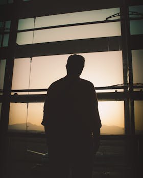 A silhouette of a man standing by a window at sunset, capturing the serene atmosphere of Izmir Airport.