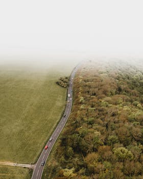 航拍镜头中，车辆行驶在雾气缭绕、树木葱郁的乡村道路上