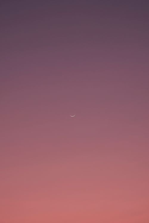 Free A minimalist view of a crescent moon set against a colorful twilight sky. Stock Photo