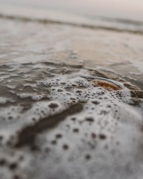 Detailed view of ocean waves and foam on sand at the beach, capturing a serene summer moment.