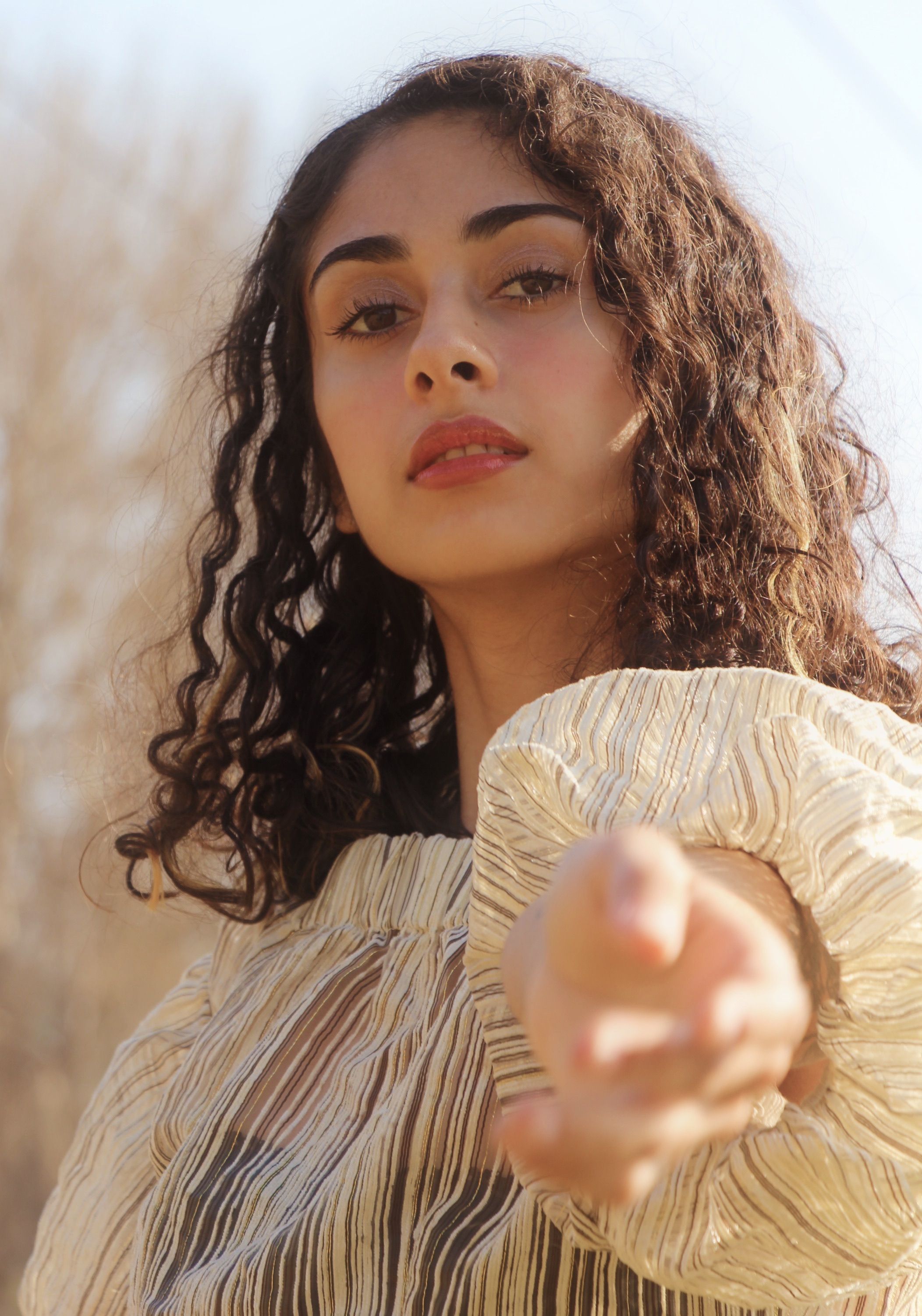 Sunlit portrait of a young woman extending her hand, wearing a striped blouse. Warm and inviting.
