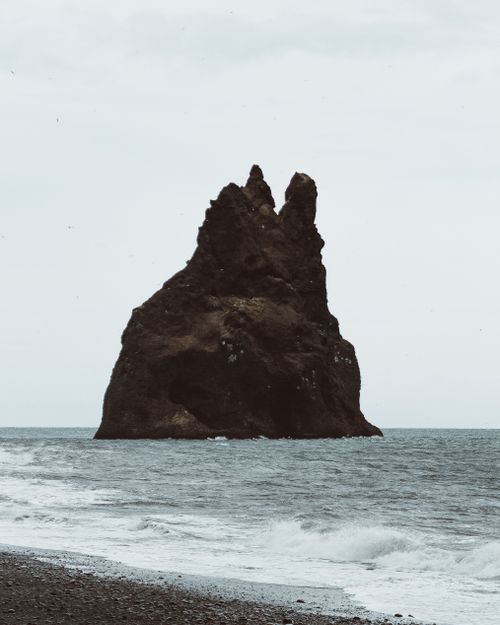 Free Captivating view of a solitary rock formation in the ocean at dusk, with waves crashing on the shore. Stock Photo