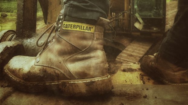 Close-up of a muddy work boot on a construction site, showcasing industrial strength and durability.
