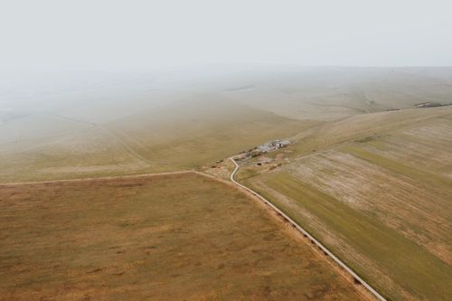 Free A serene aerial view of a foggy countryside landscape with a small road cutting through vast fields. Stock Photo