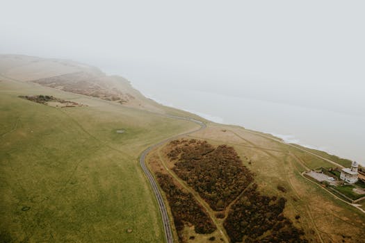 A serene aerial shot capturing a foggy coastline with a winding road amidst rolling hills.