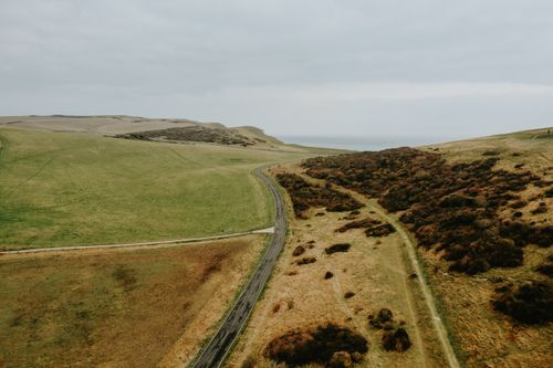 Free Aerial shot of a coastal countryside landscape with winding road and open fields against the sea. Stock Photo