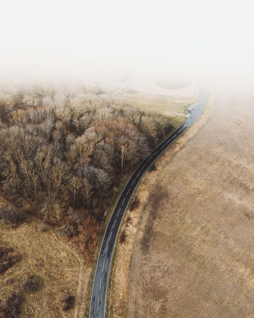 A misty aerial scene showing a winding road through fall countryside with trees and grassland.