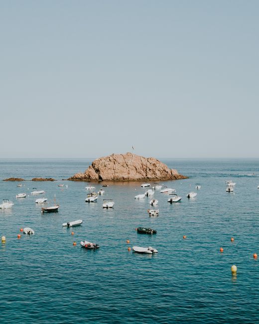 Tranquil scene of boats anchored near a rocky island on a calm sea.