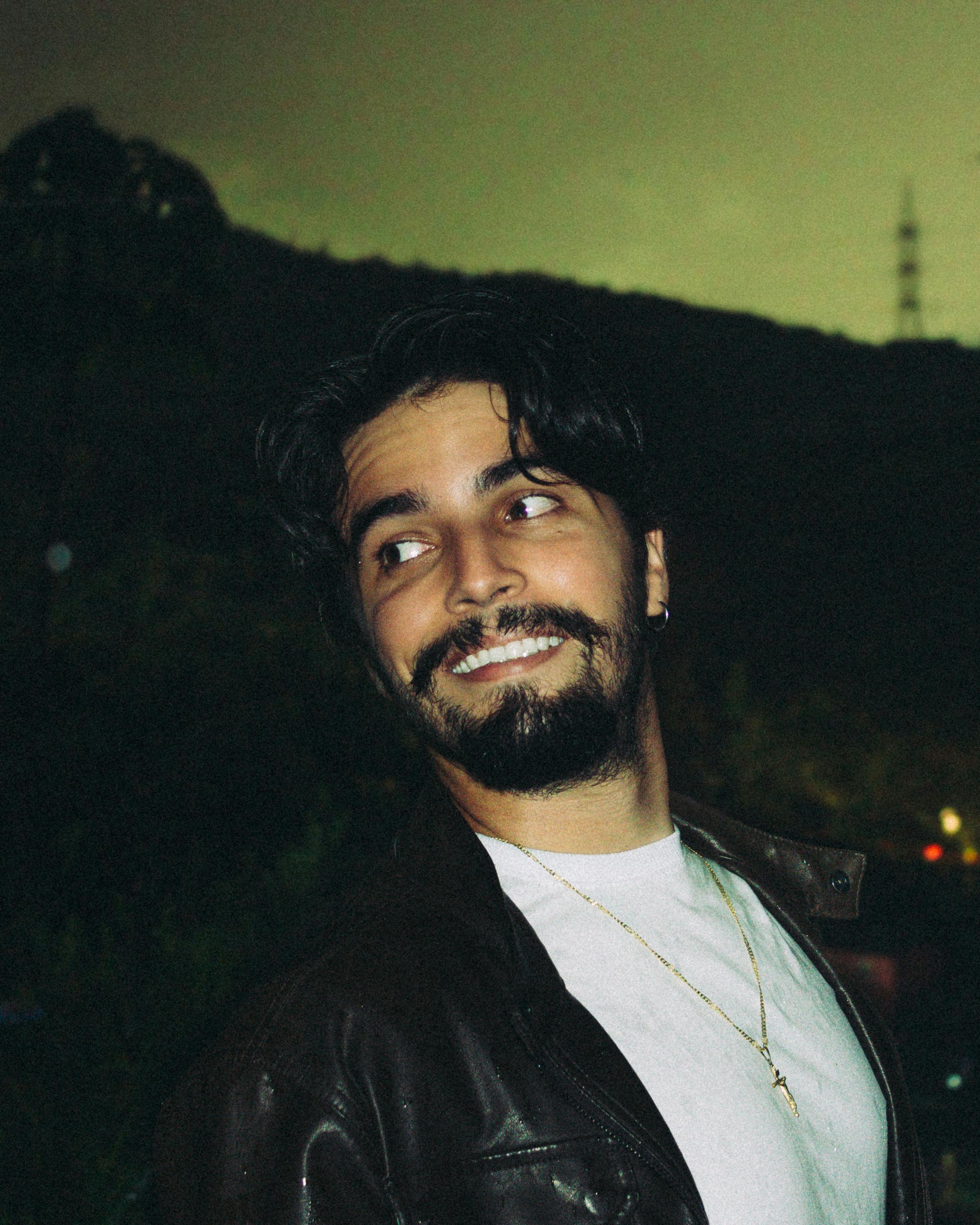 A cheerful man in a leather jacket looking sideways against a nocturnal backdrop.