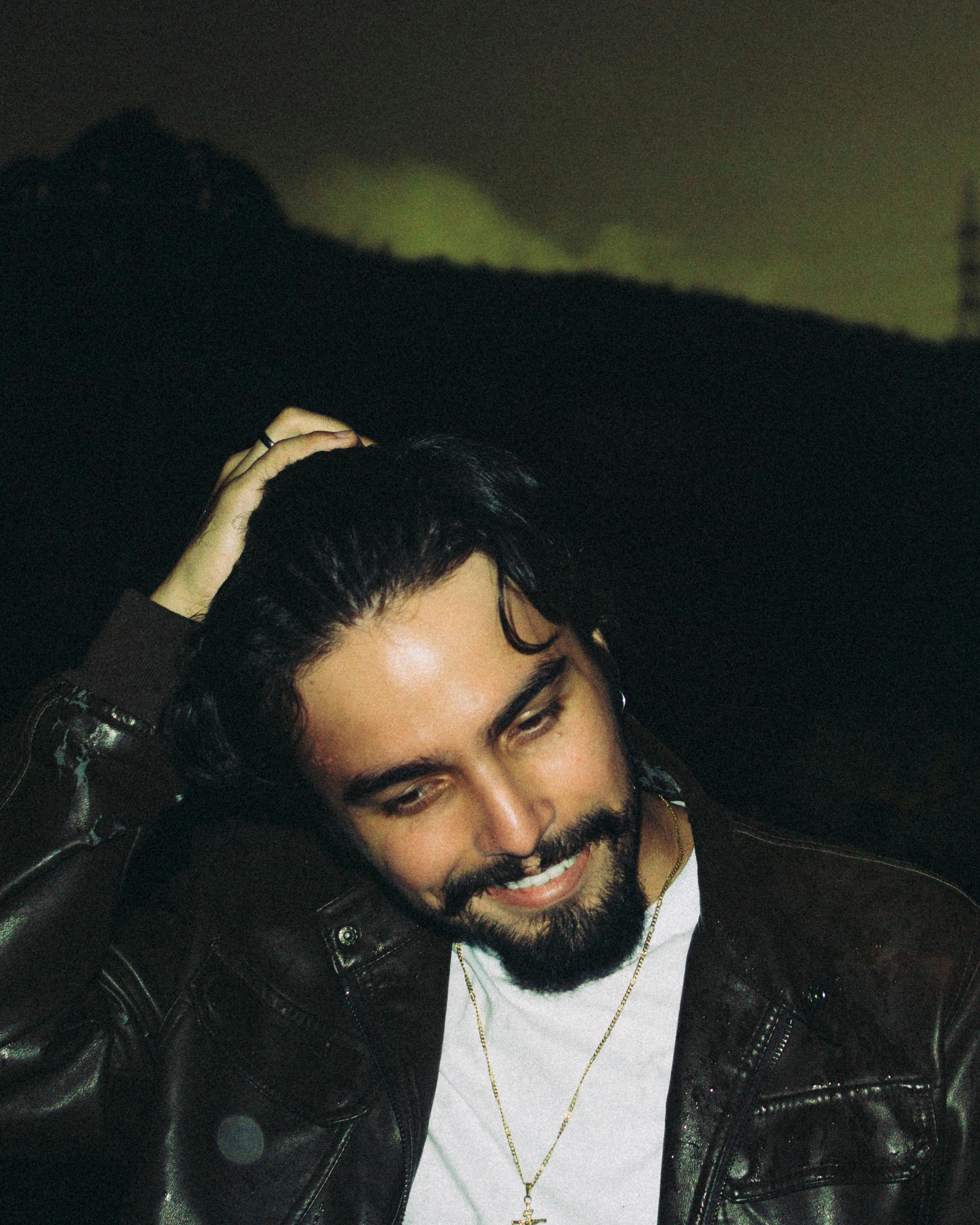 A candid portrait of a man smiling, wearing a leather jacket outdoors at night.